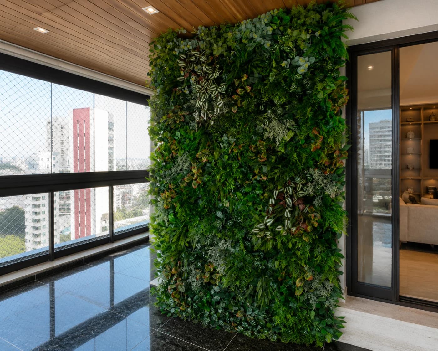 Jardim vertical permanente cobrindo a parede de uma varanda de apartamento, com forro de madeira e vista para a cidade